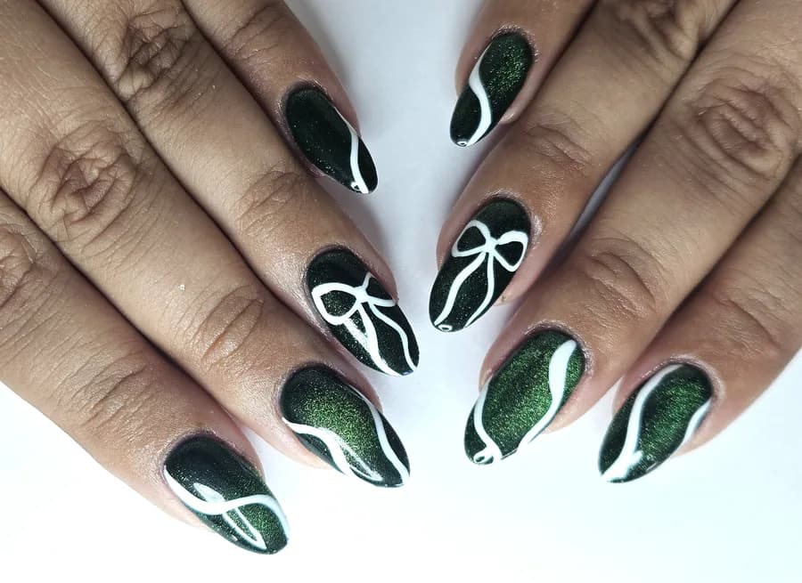 Dark green cat eye nails with a glowing shimmer, finished with white line art bows and swirls.