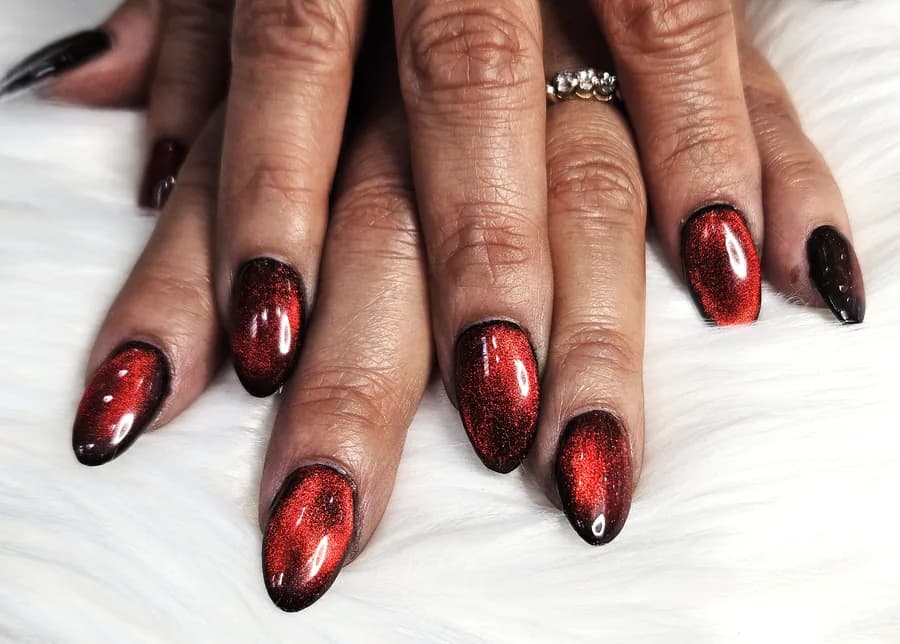 Red and black cat eye nails on almond shaped nails, each nail showing a bright band of light across the color.